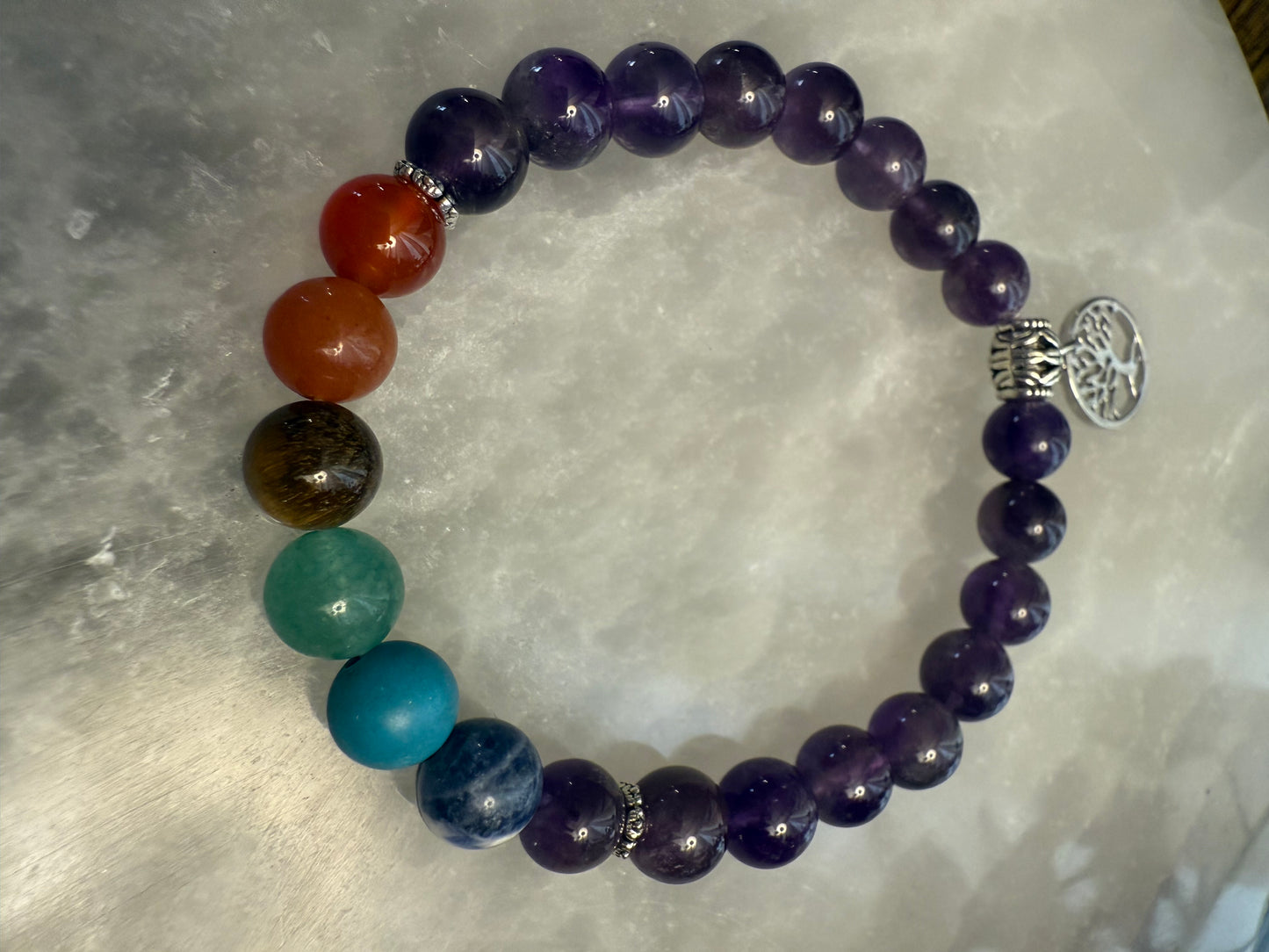 Multicolored Amethyst Chakra Balance Bracelet with a silver tree of life charm on a textured surface