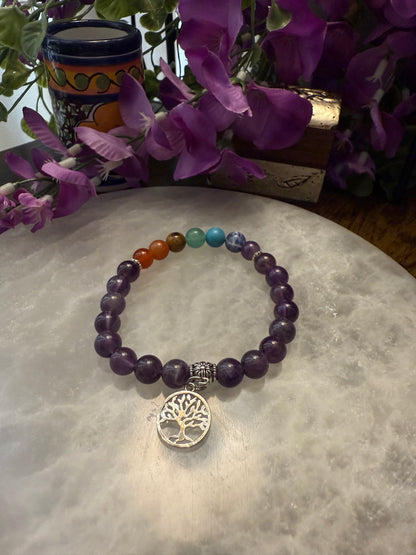 Amethyst Chakra Balance Bracelet with a tree of life charm on a textured surface with purple flowers in the background