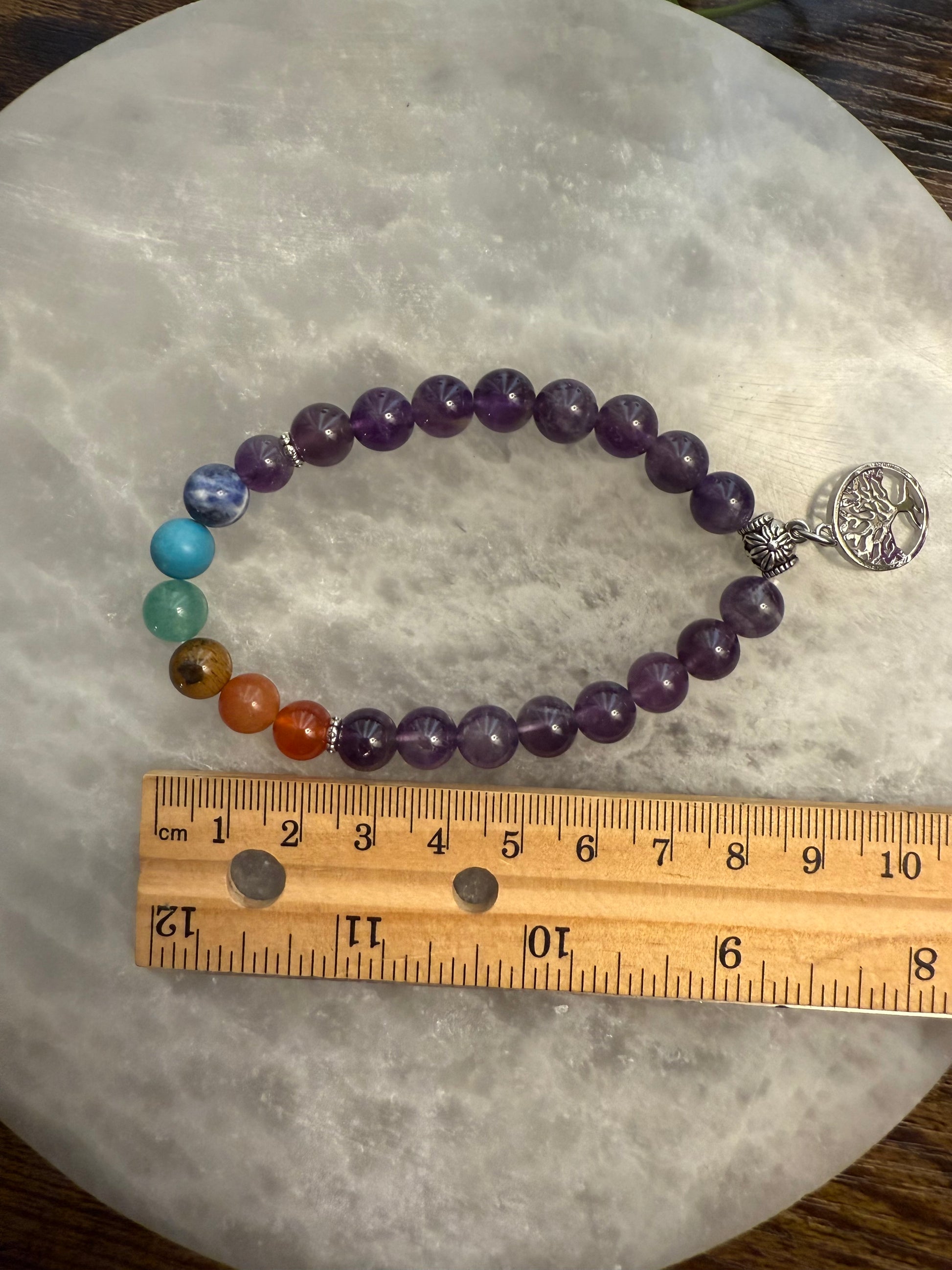 Amethyst Chakra Balance Bracelet with a tree of life charm on a gray surface, measured against a wooden ruler.