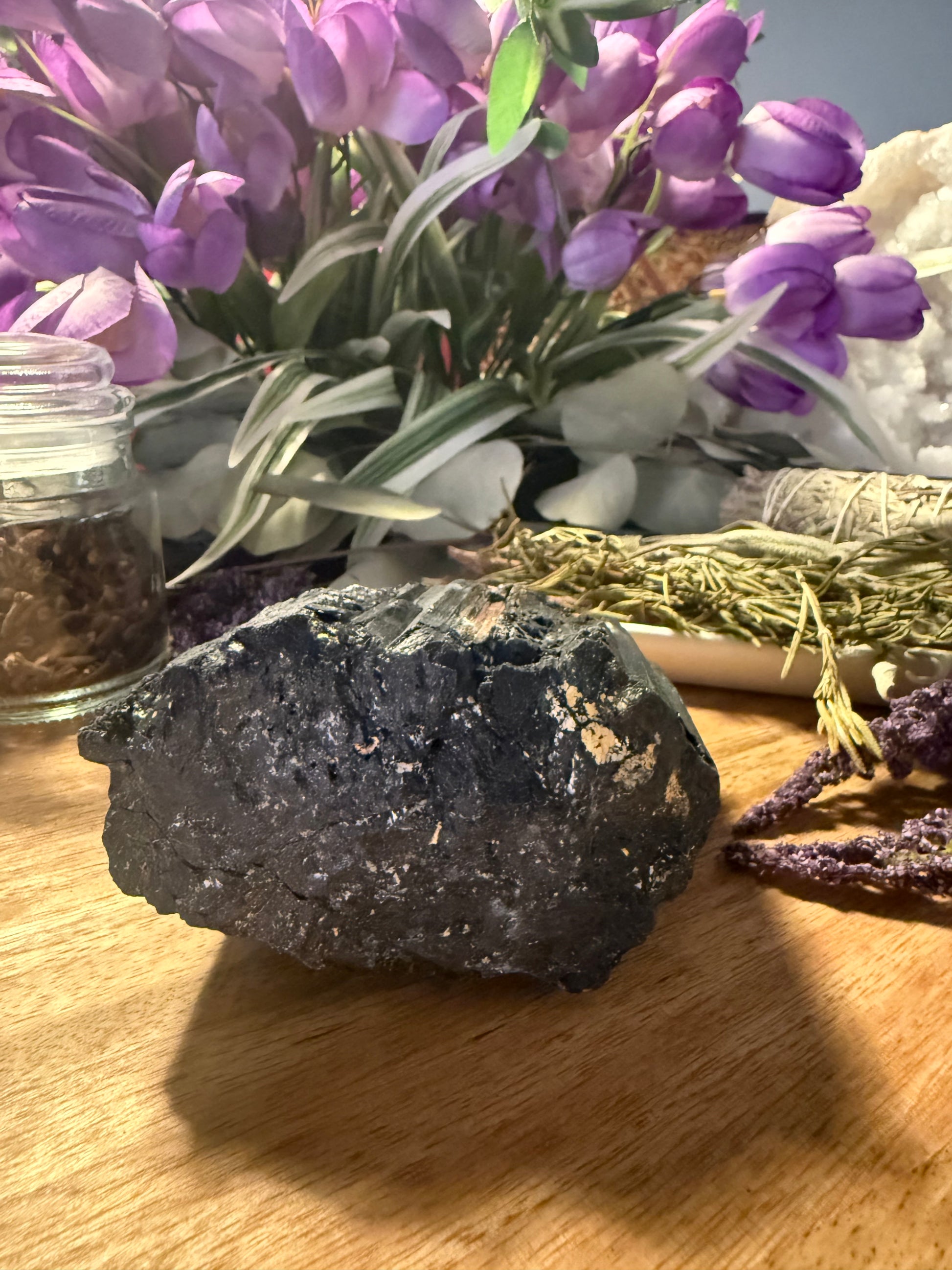 Raw Black Tourmaline on a wooden surface with purple flowers and decorative elements in the background