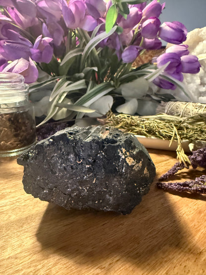 Raw Black Tourmaline on a wooden surface with purple flowers and decorative elements in the background