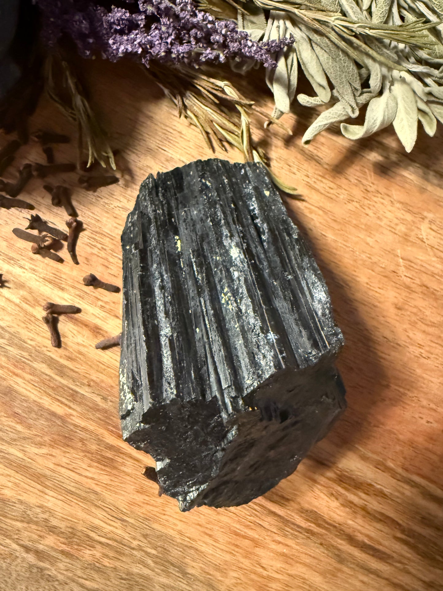 Raw Black Tourmaline on a wooden surface with herbs