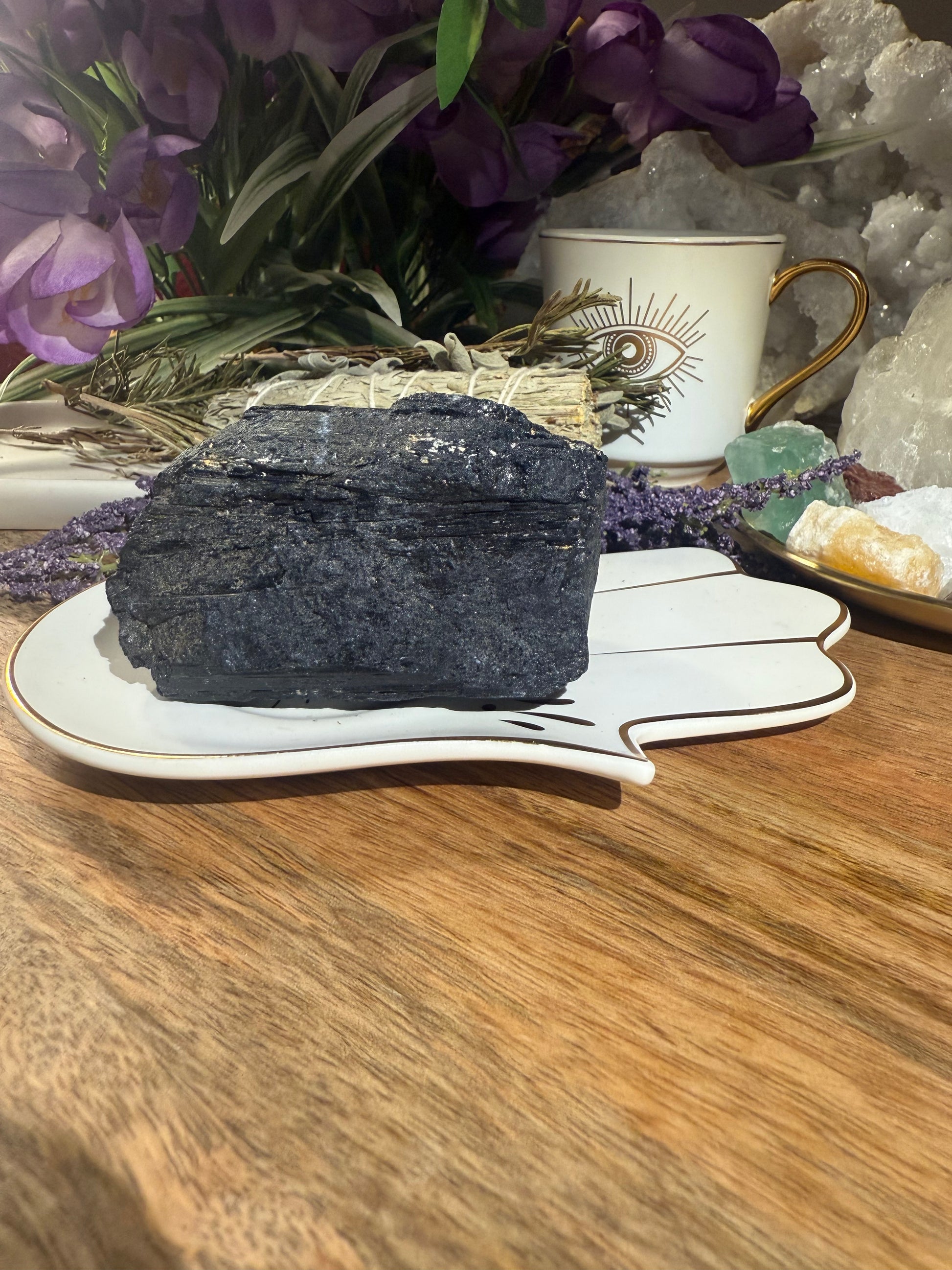 Decorative setting with a dark crystal on a leaf-shaped stand, surrounded by flowers and a small cup.