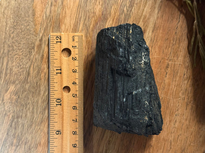 Black rock or coal sample next to a wooden ruler on a wooden surface