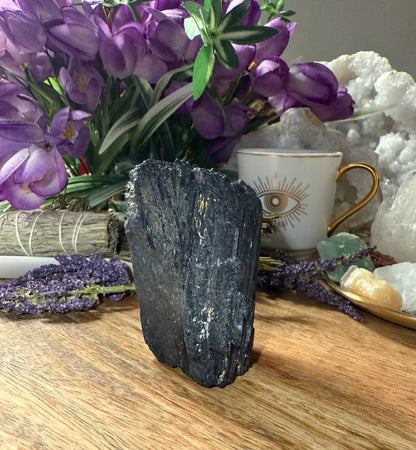 Black crystal on a wooden surface with purple flowers and a cup in the background