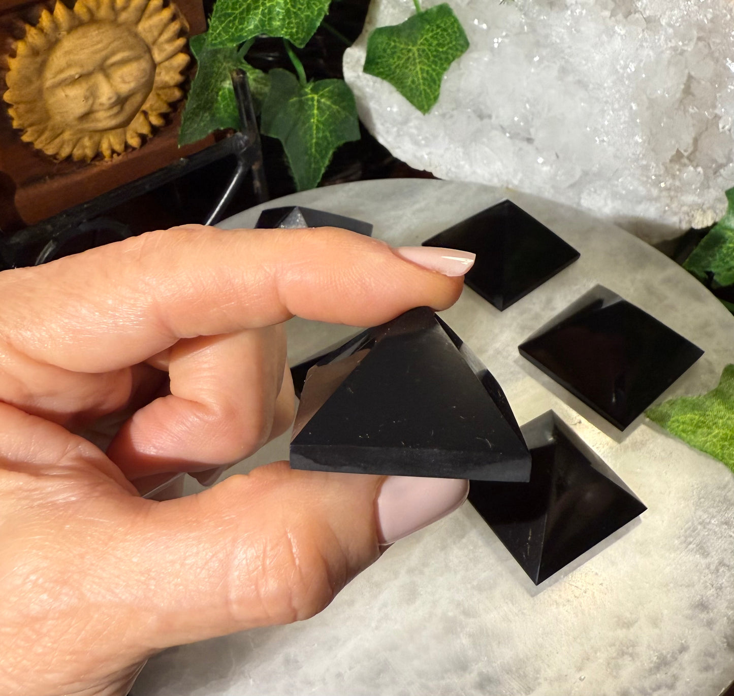 Hand holding a black Shungite Pyramid stone with a decorative background