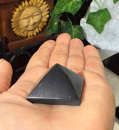 Hand holding a black Shungite Pyramid stone with a decorative background