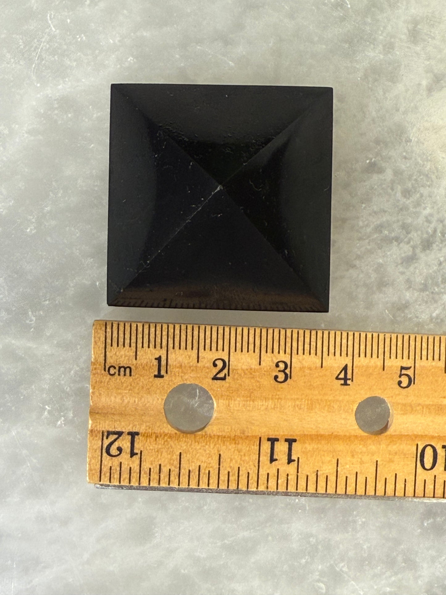 Black Shungite Pyramid stone next to a wooden ruler on a gray surface