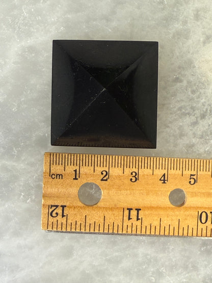 Black Shungite Pyramid stone next to a wooden ruler on a gray surface