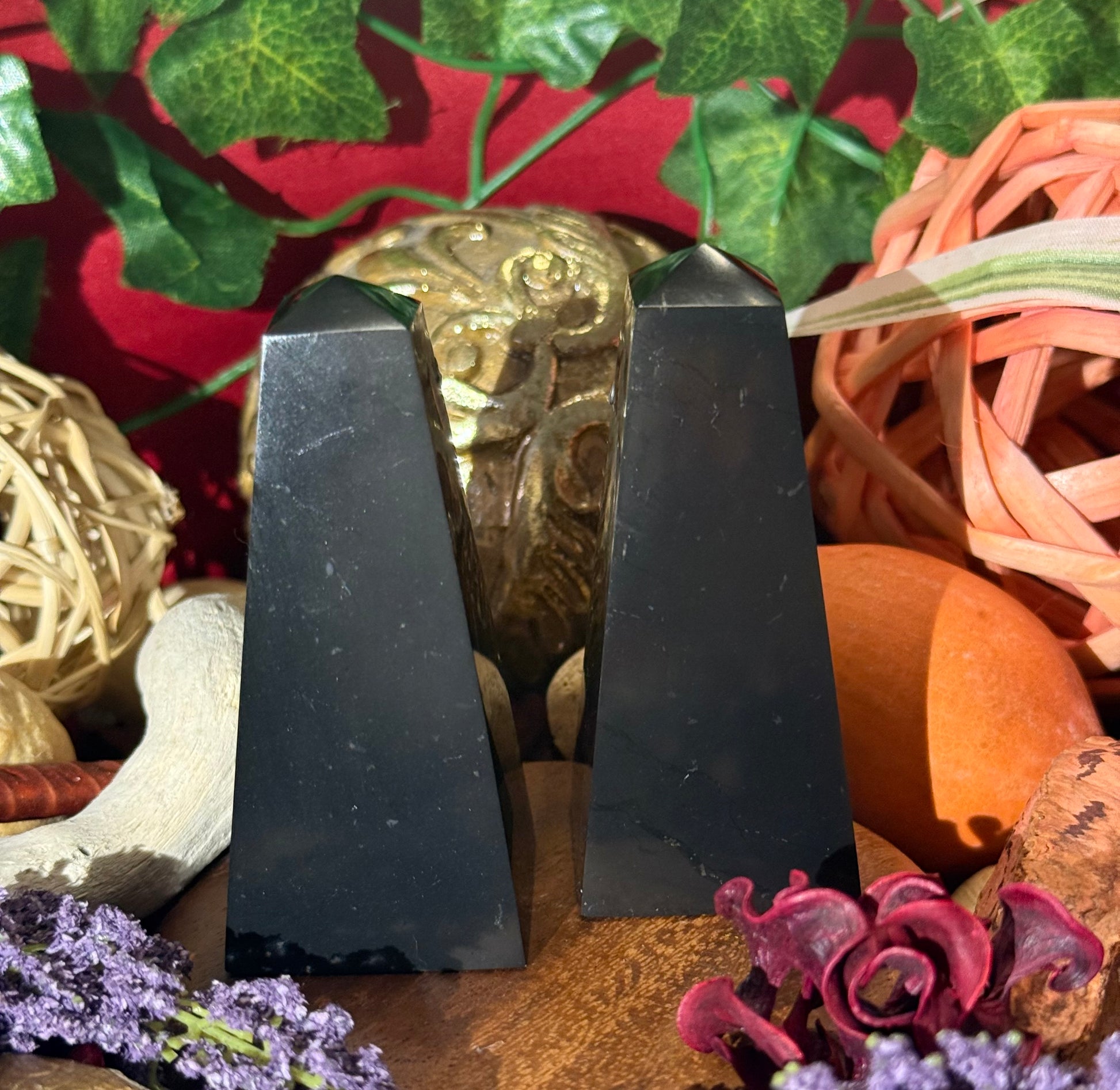 Two Shungite Pyramid stones on a decorative background with plants and flowers.