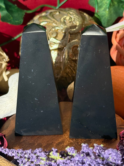 Two black Shungite Pyramids stone on a wooden surface with a decorative background.