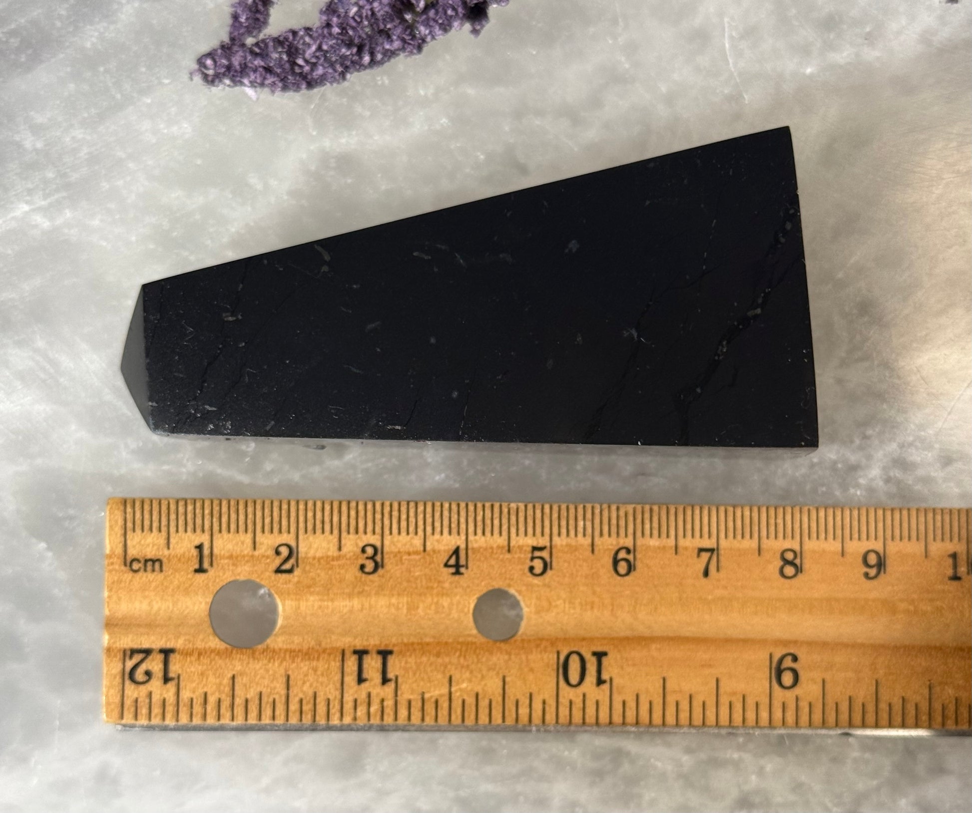 Black Shungite Pyramid next to a wooden ruler on a textured surface